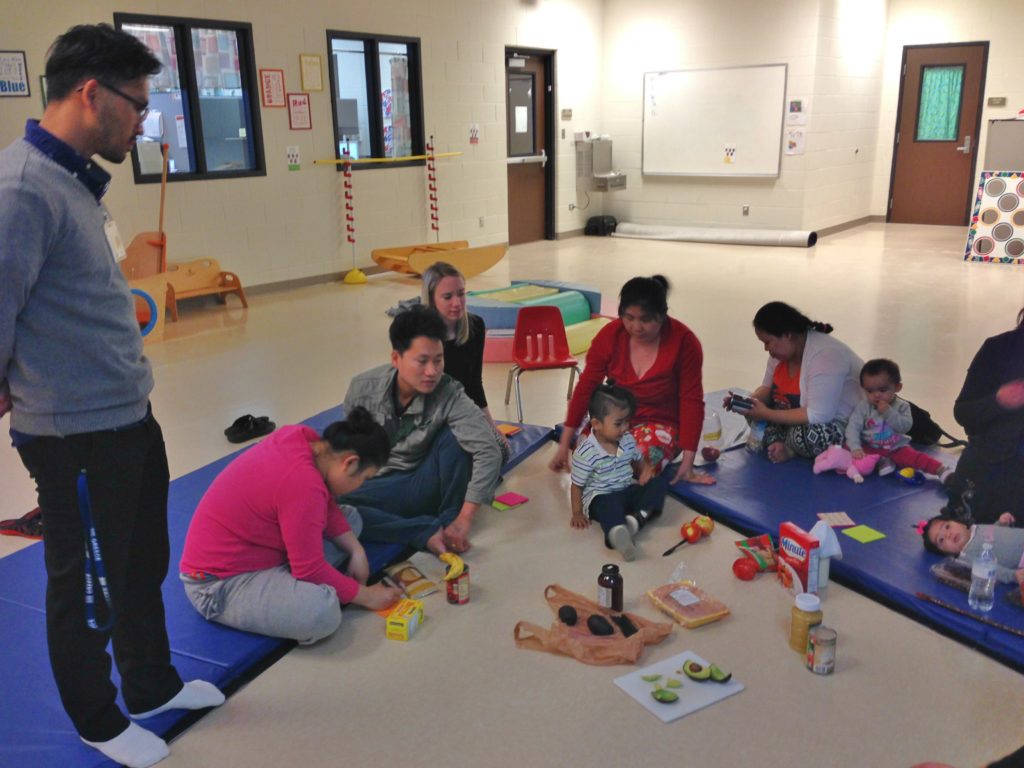 Parents and their young children look at various healthy foods in the ECFE classroom