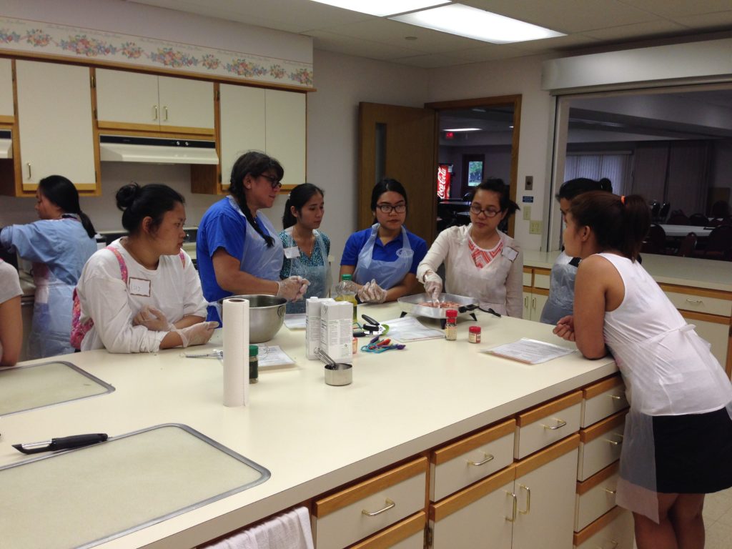 Women are gathered around a kitchen counter observing a cooking demonstration