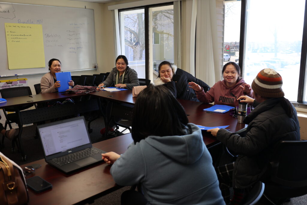 A group of participants sit around a table and talk at the KOM office.