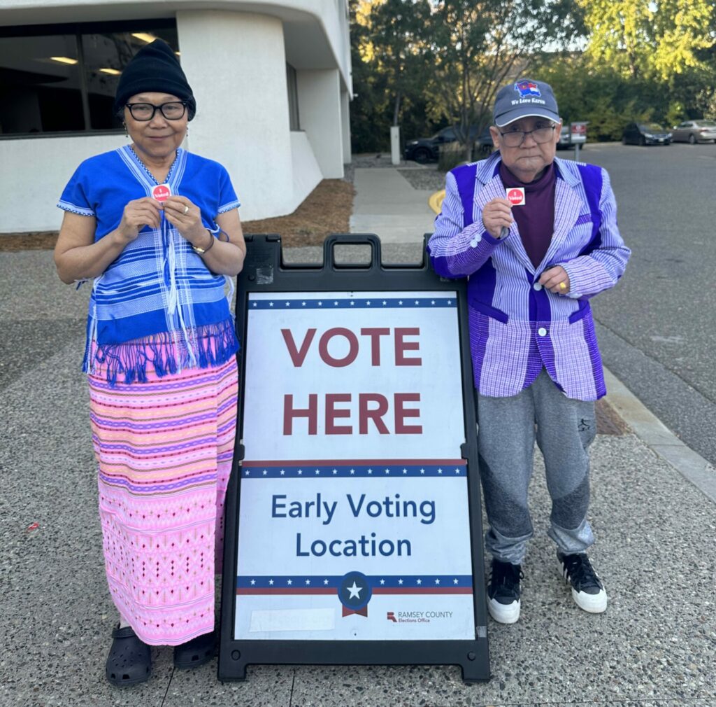 Two Karen elders pose with their "I Voted" stickers next to the Vote Here: Early Voting Location sign.