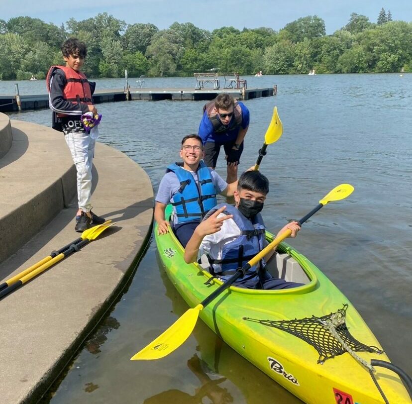 A volunteer and youth seated in a kayak on Lake Como, with one youth standing on the shore.